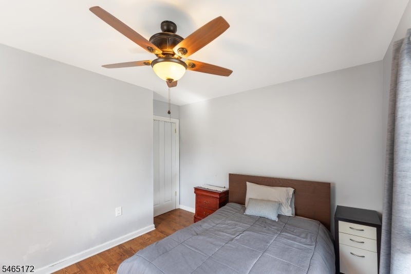 Bedroom with a gray-quilted bed, wood headboard, and ceiling fan with light.