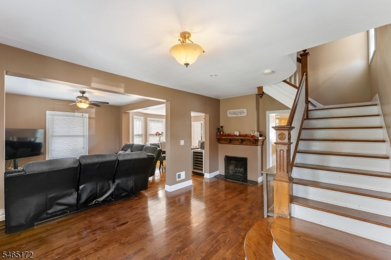 Living room with leather sectional, hardwood floors, fireplace, and prominent staircase.