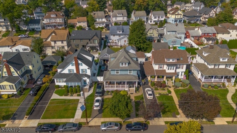 Aerial view of a residential street with varied homes, front yards, and parked cars.