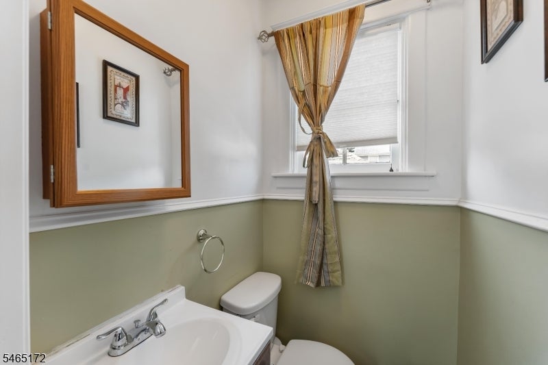 Bathroom with a white sink, toilet, wood-framed mirror, and tied-back window curtains.