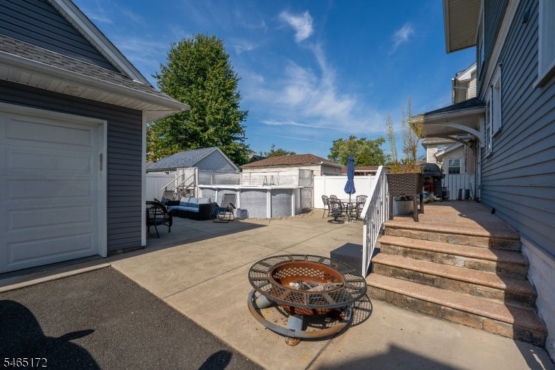 Paved patio with a fire pit, outdoor seating, garage, and steps beside the house.