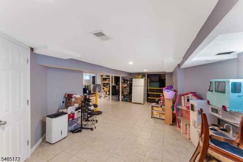 Finished basement with tiled flooring, storage shelves, exercise equipment, and children’s play furniture.