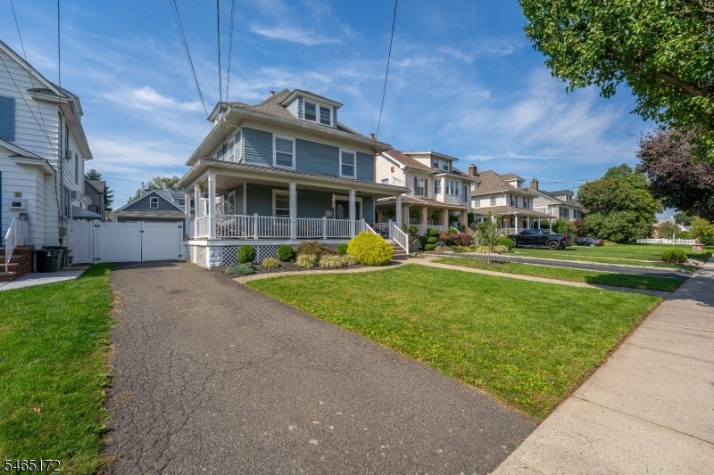Blue-gray two-story house with a wraparound porch, broad front lawn, and driveway to a detached garage.