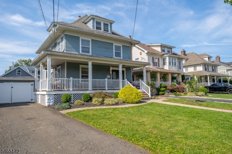 Blue two-story house with a wraparound porch, white railings, and landscaped front lawn.