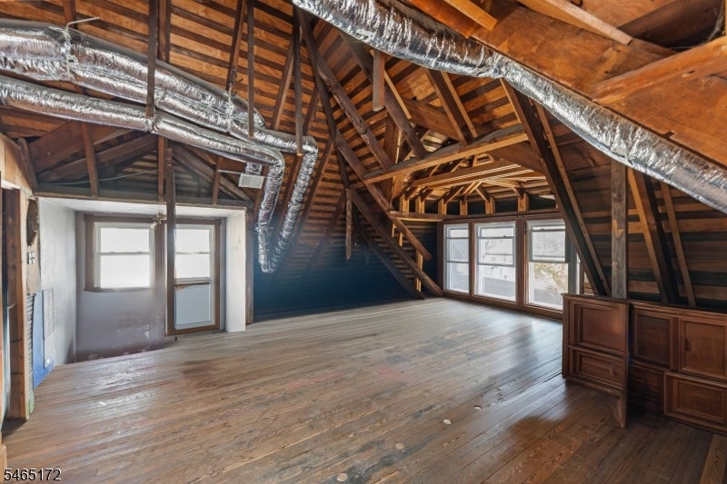 Attic with exposed wooden rafters, timber flooring, multiple windows, and built-in cabinets.