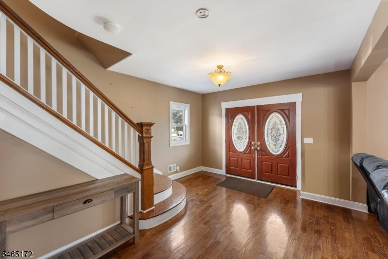 Entry foyer with hardwood floors, a wooden staircase, and double doors with oval glass panels.