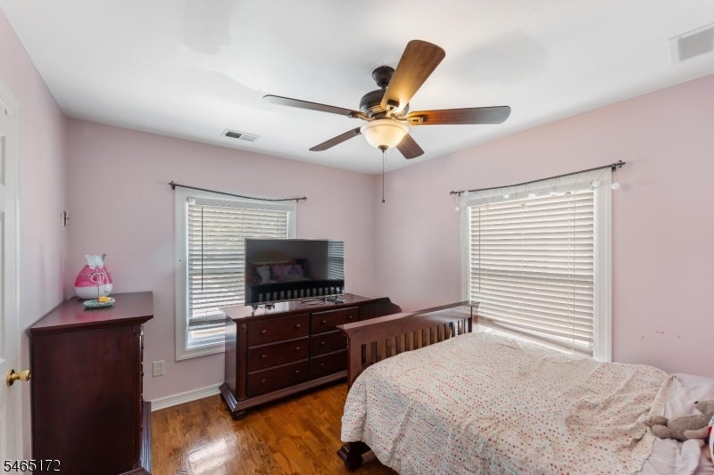 Bedroom with pale pink walls, hardwood floors, a ceiling fan, and dark wood dressers.