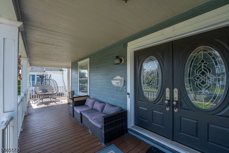Covered front porch with ornate double entry doors and cushioned wicker seating.