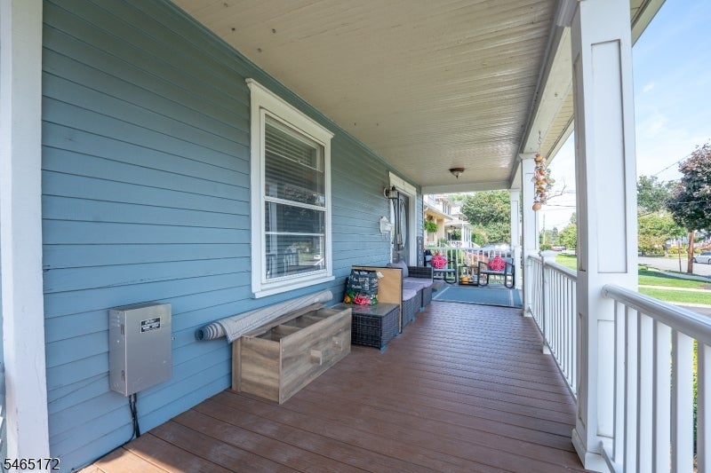 Covered porch with blue siding, white railings, wicker seating, and a wooden storage bench.