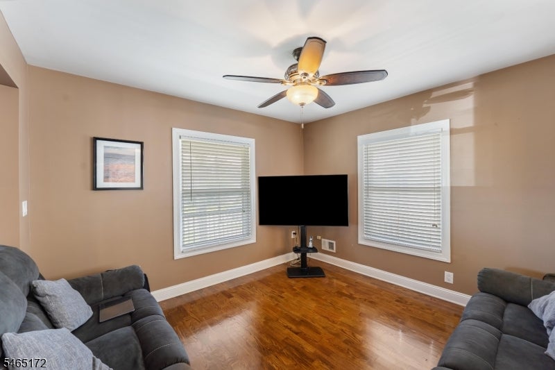 Living room with gray sofas, glossy hardwood floors, two shuttered windows, and a ceiling fan.