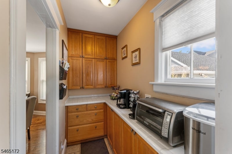 Kitchen with wood cabinets, tiled counters, and small appliances beside a window.