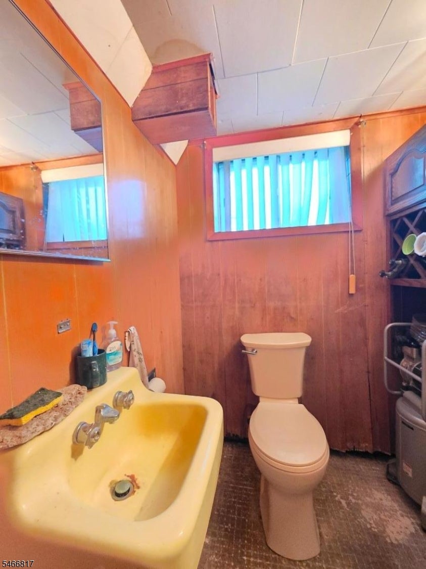 Bathroom with a yellow sink, toilet, wood-paneled walls, and a high window with blue blinds.
