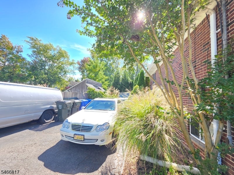 Brick house beside a driveway with a white sedan, landscaping, and a detached garage.