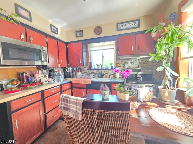 Kitchen with red wood cabinets, stainless steel appliances, and a sunlit dining nook.