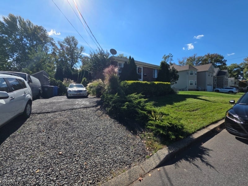 Brick house behind shrubs, beside a gravel driveway and lawn.