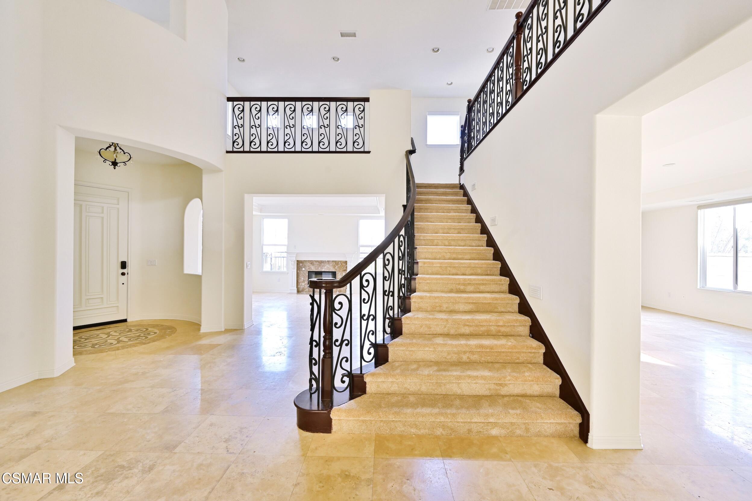 Two-story foyer with a carpeted staircase, ornate iron railings, and beige tile floor.