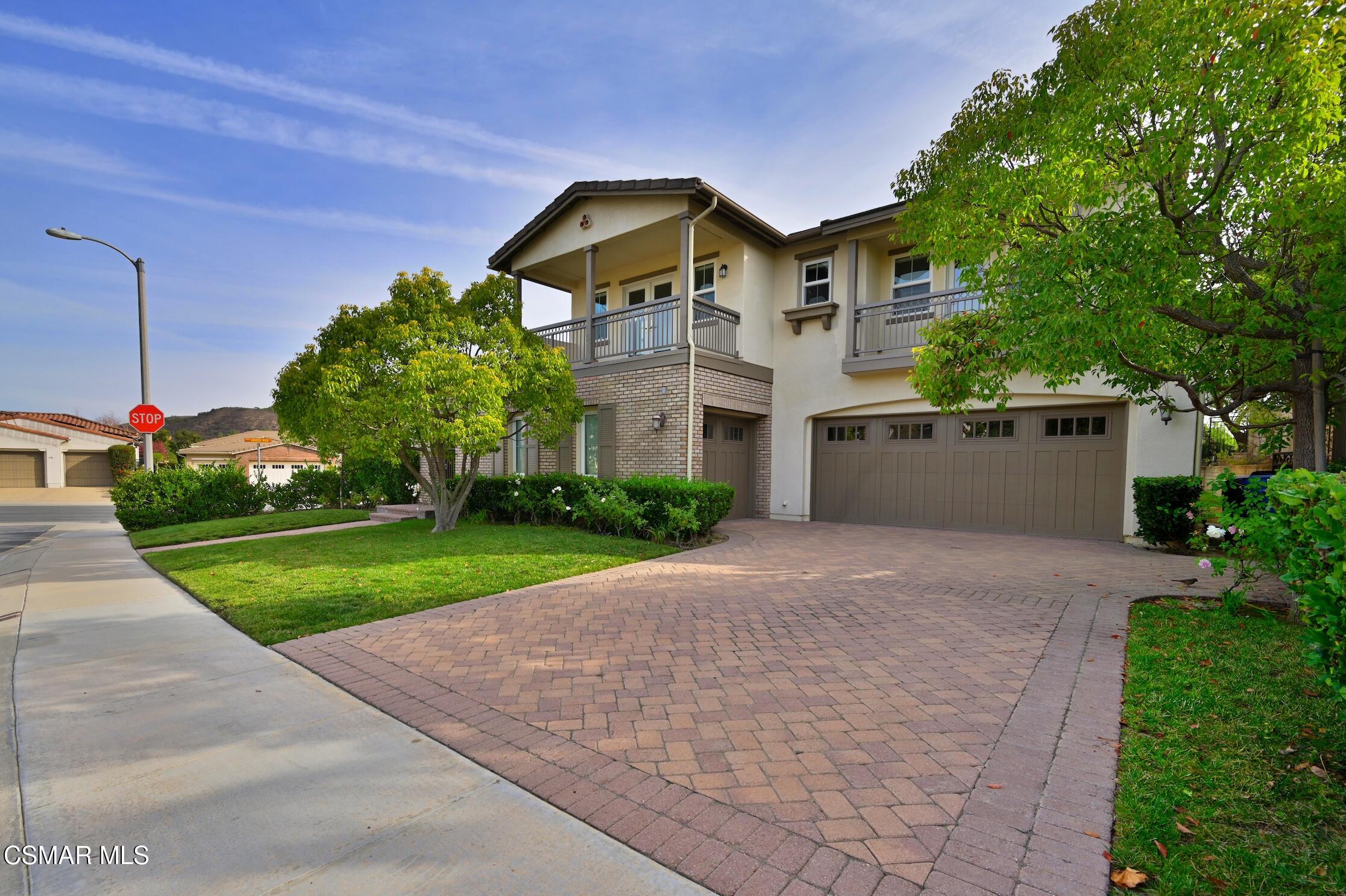 Two-story home with balconies, a two-car garage, and a broad brick-paver driveway.