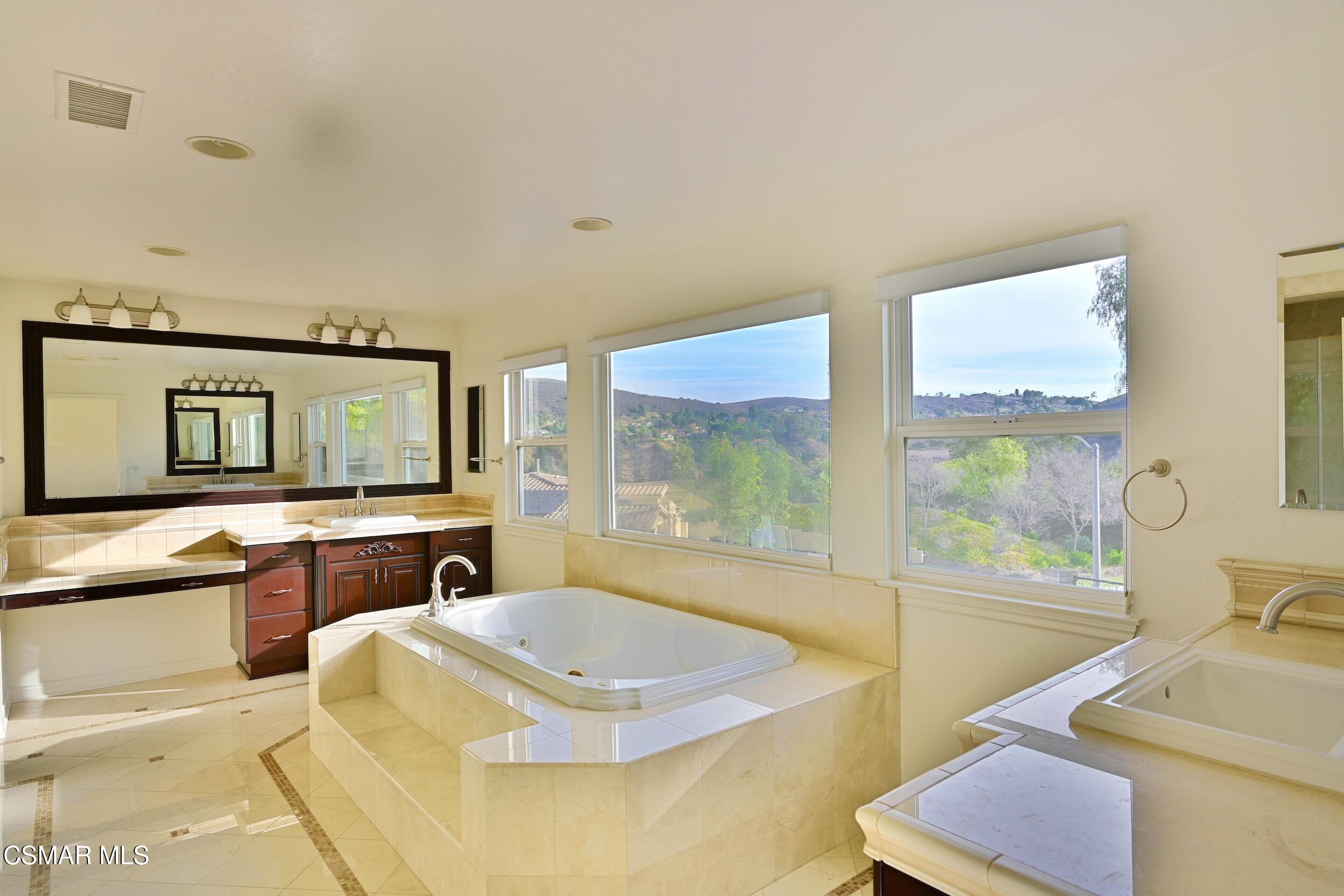Bathroom with a built-in corner tub, double vanity, and large windows overlooking green hills.