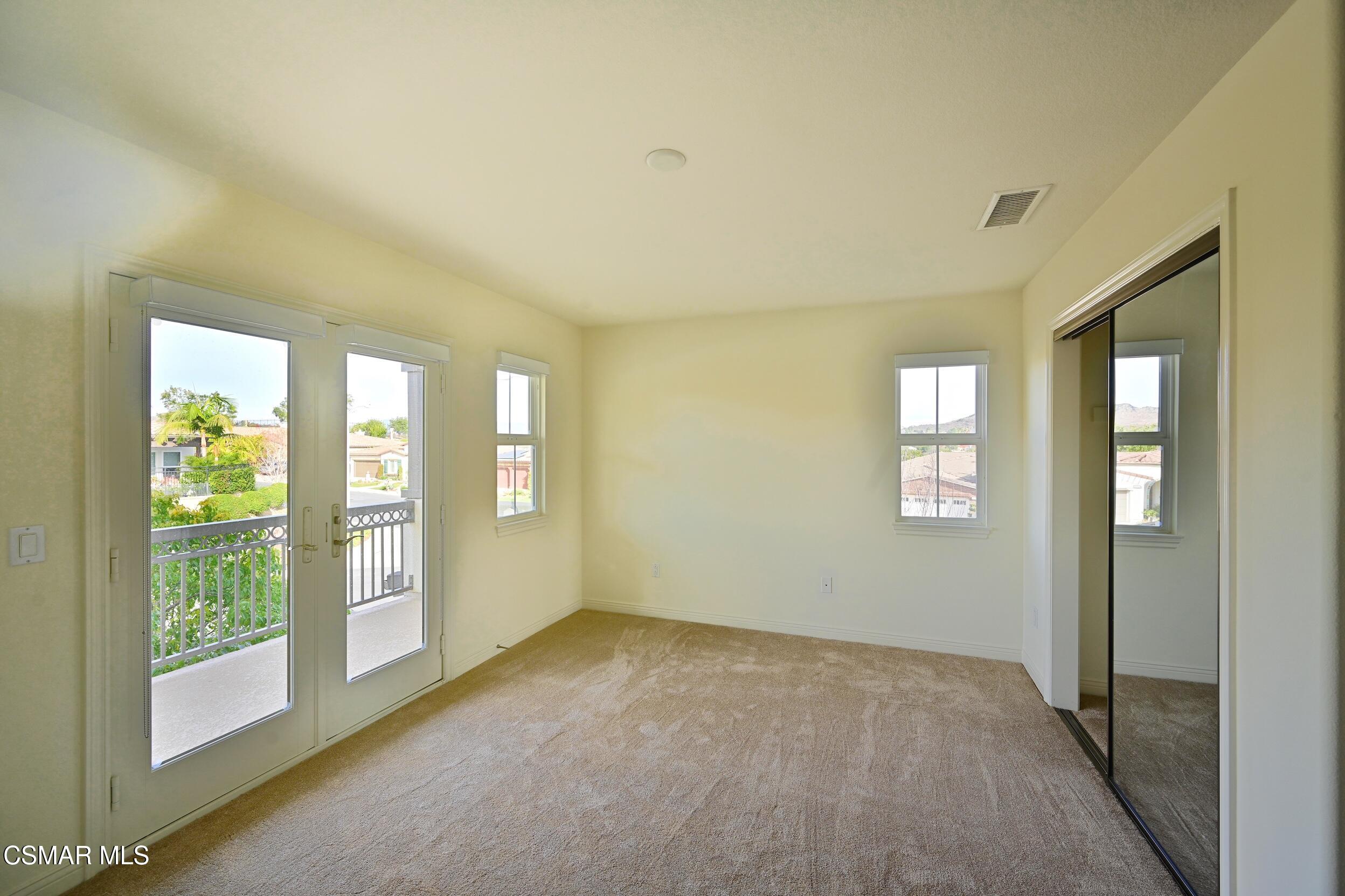 Empty carpeted bedroom with mirrored closet doors and glass doors opening to a balcony.