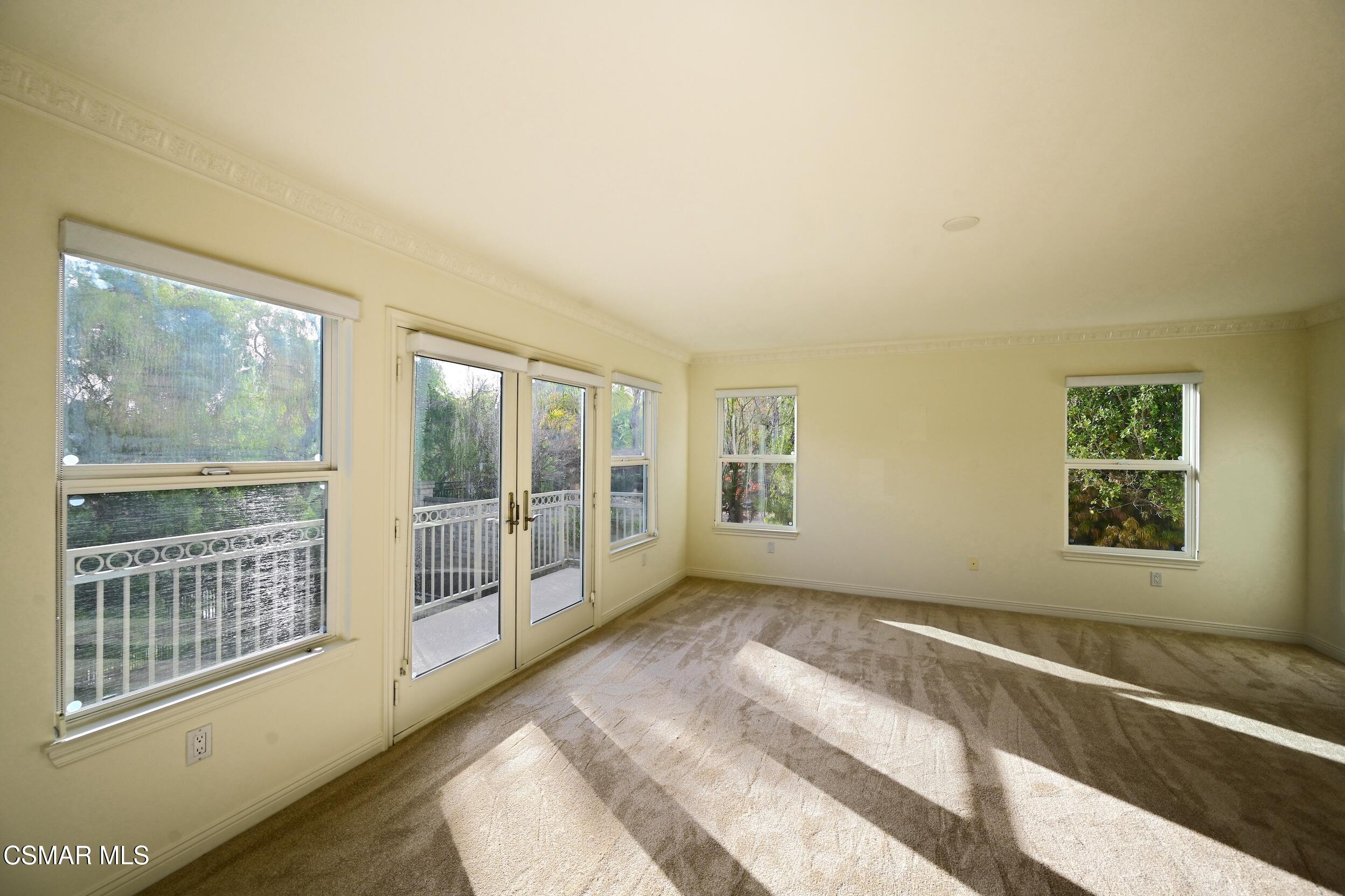 Empty carpeted room with glass doors to a balcony and sunlight falling across the floor.