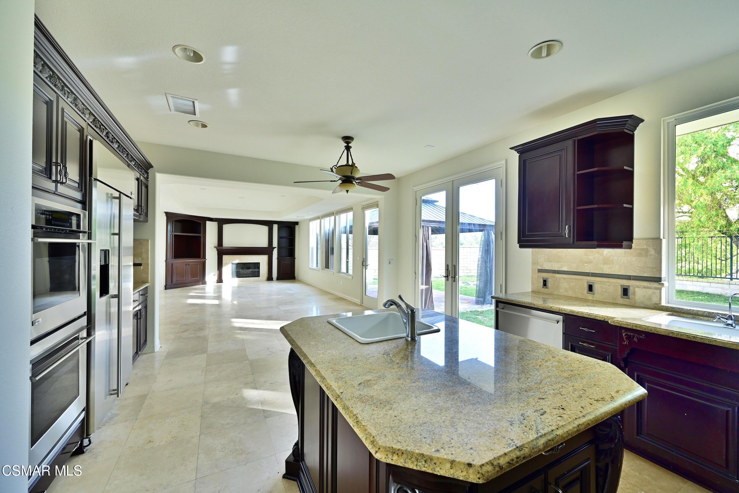 Kitchen with dark cherry cabinets, stainless steel appliances, and a large granite island overlooking a living room.