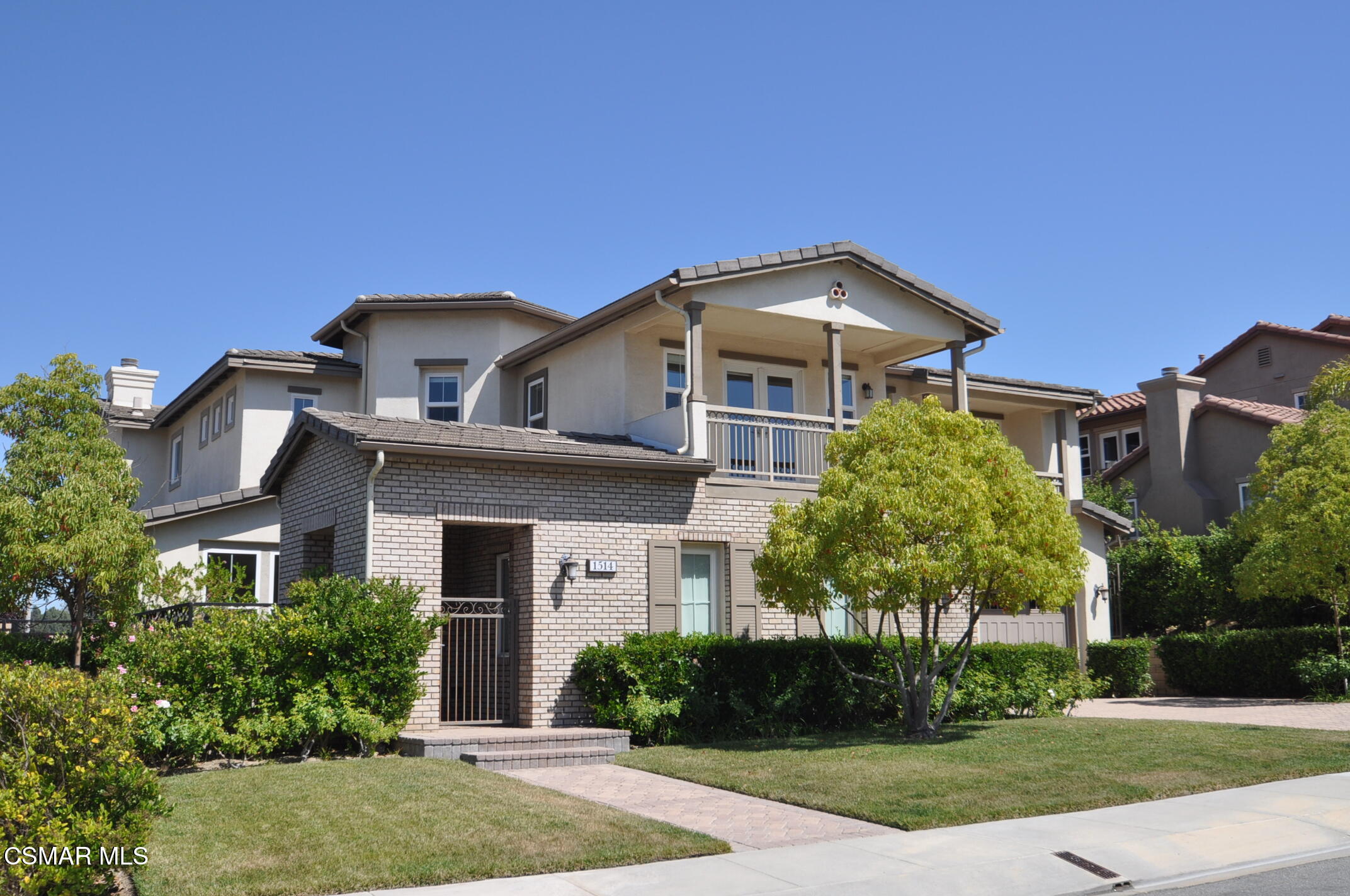 Two-story home with a light brick facade, covered balcony, and landscaped front lawn.