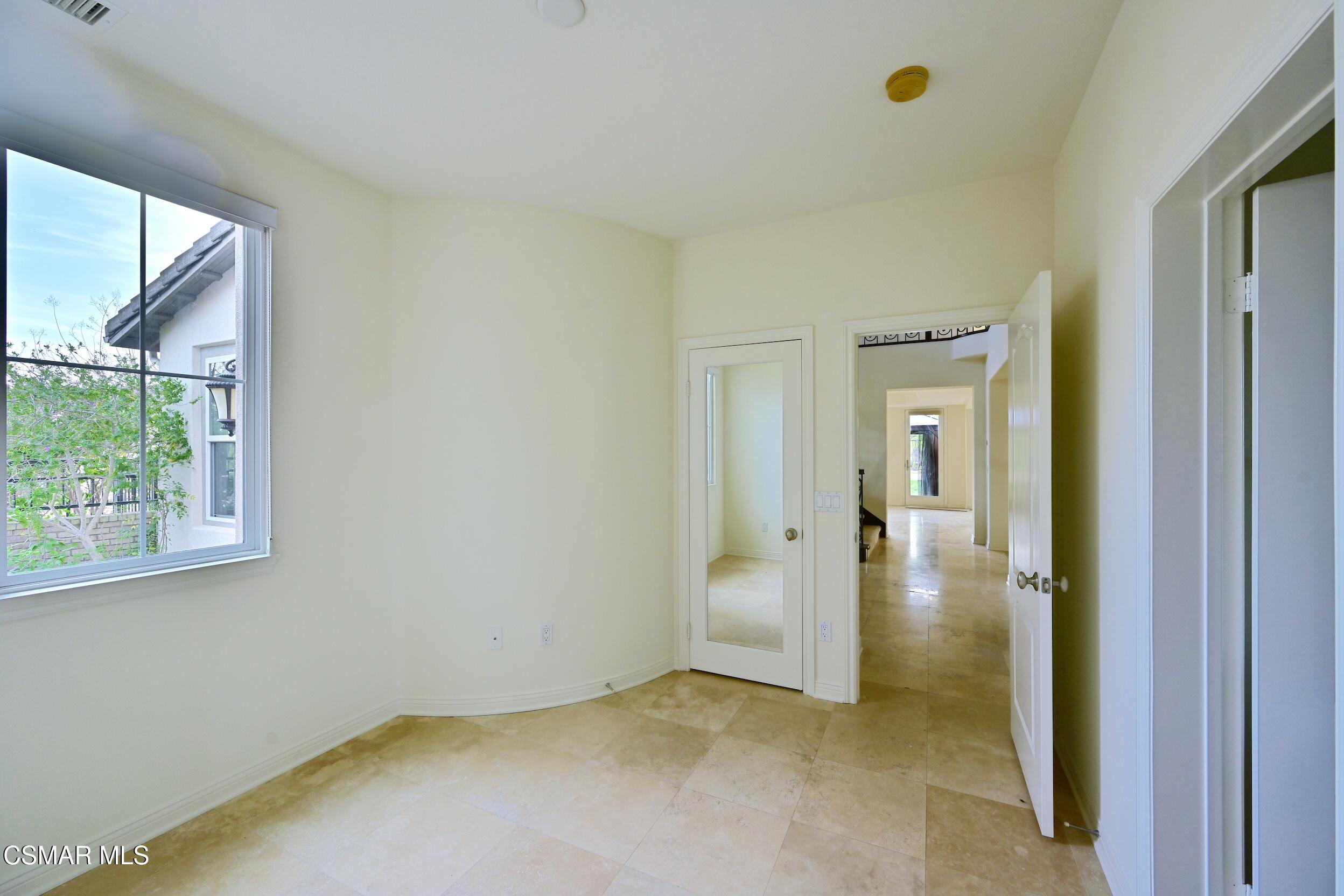 Empty room with beige tile flooring, a large window, and open doorways to a hallway.