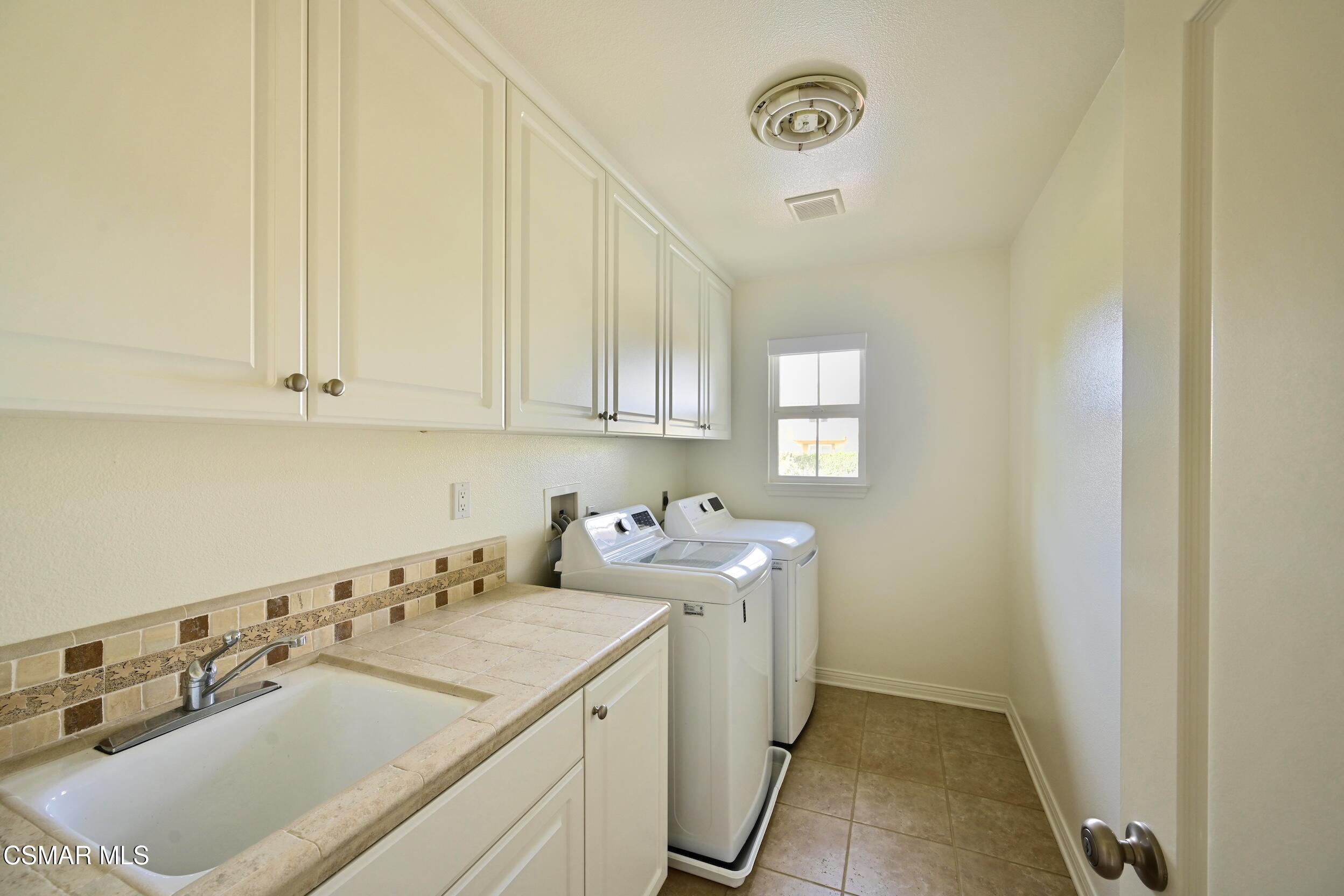 Laundry room with white cabinets, a tiled utility sink counter, and a washer and dryer.