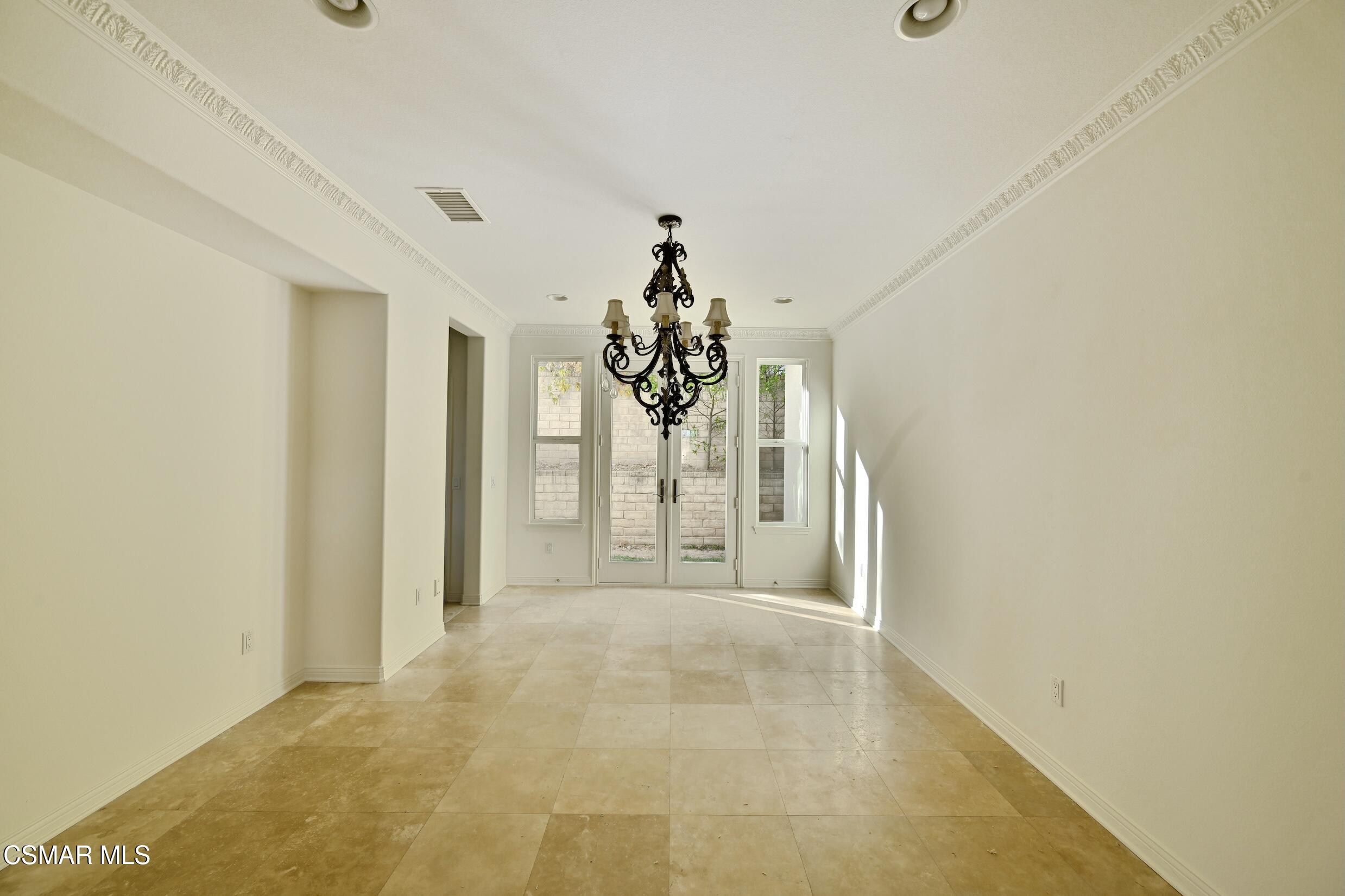 Empty dining room with beige tile floors, an ornate chandelier, and French doors.