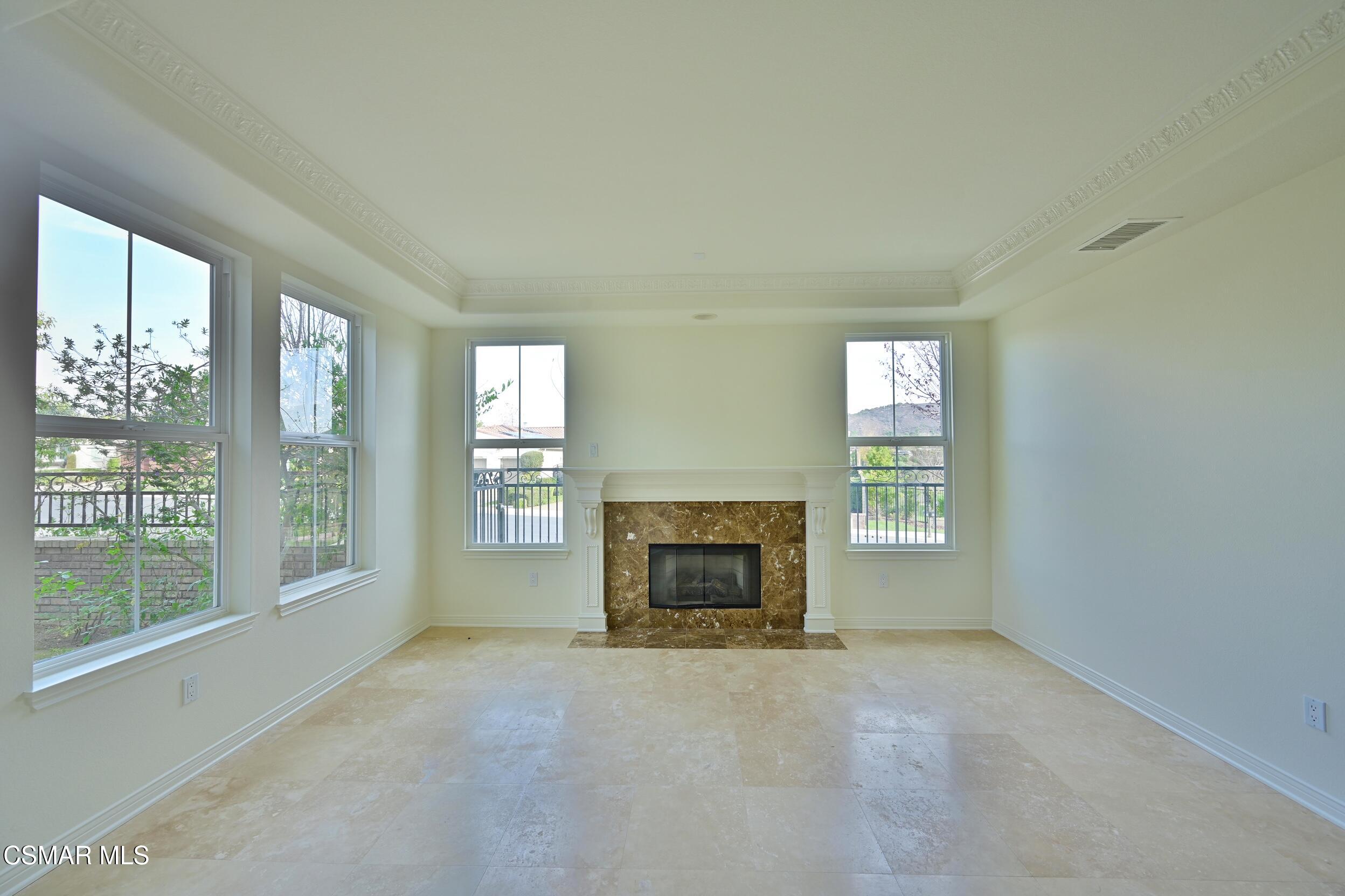 Vacant living room with a marble fireplace, large windows, and pale tile flooring.