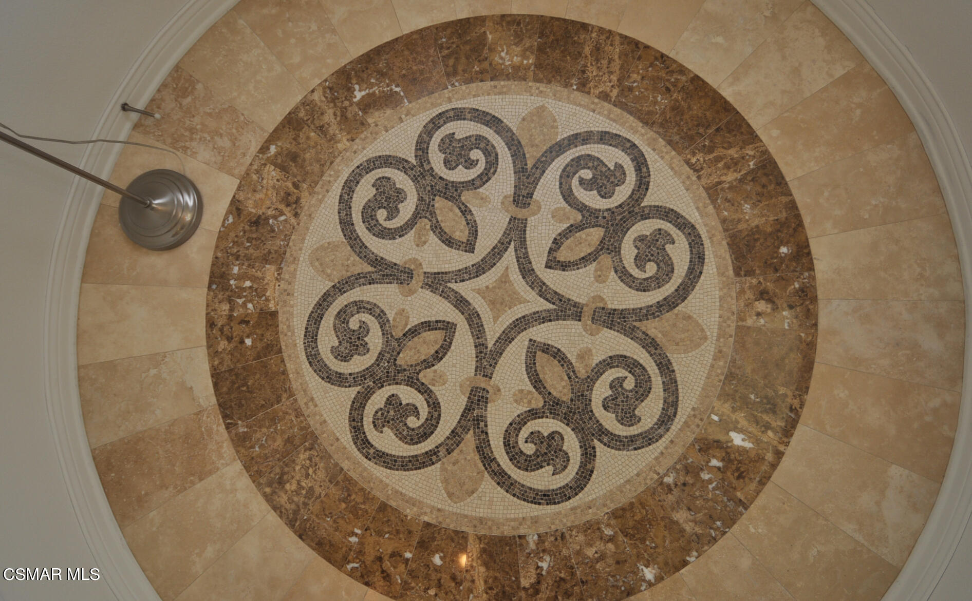 Circular scroll-pattern mosaic tile medallion in a tan stone bathroom floor.