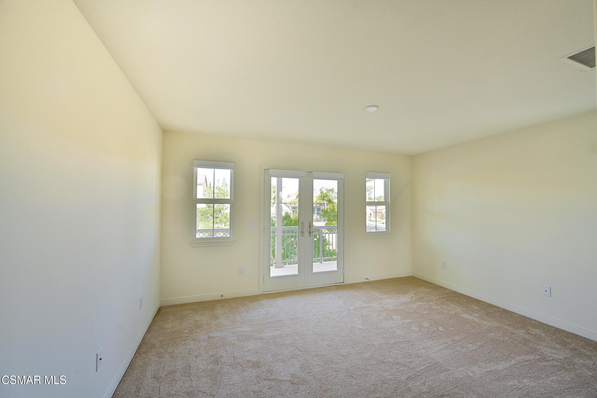 Vacant carpeted room with glass double doors opening to a balcony and windows on either side.