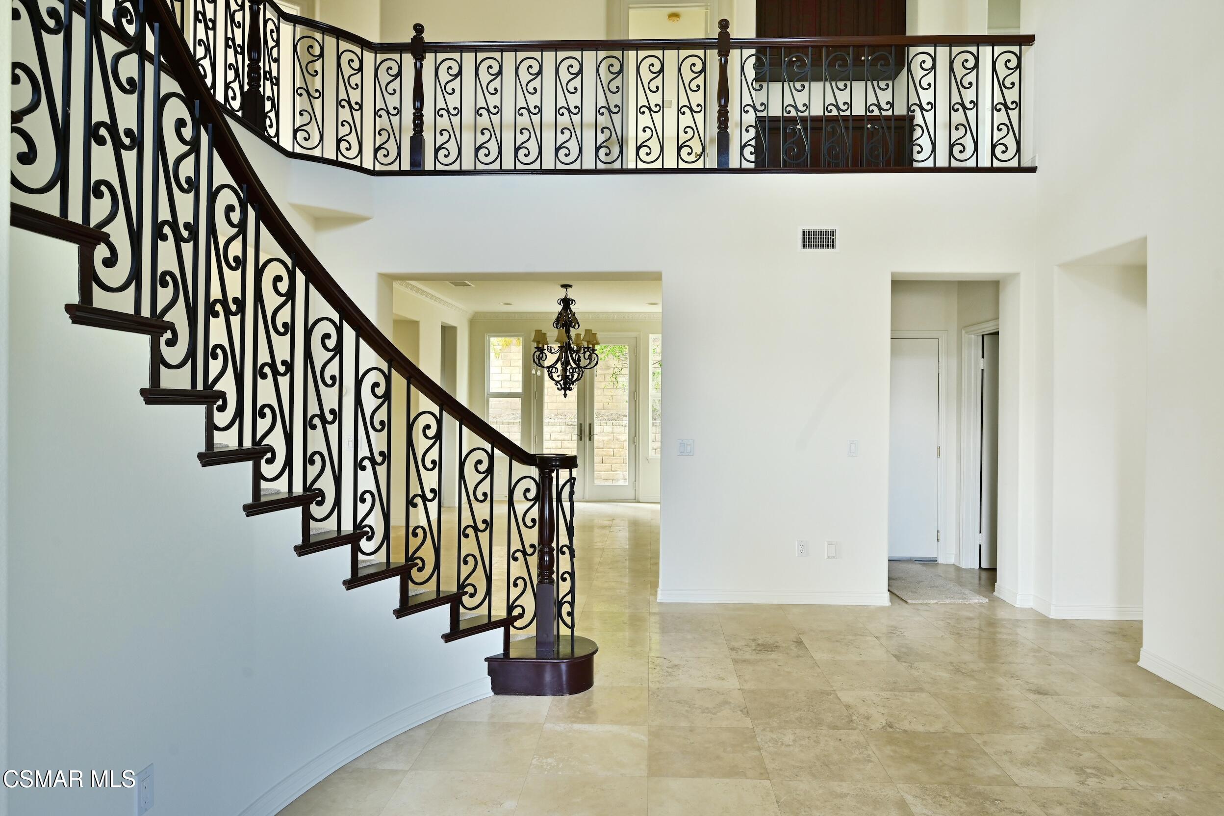 Two-story entry hall with a sweeping wrought-iron staircase, chandelier, and beige tile floor.