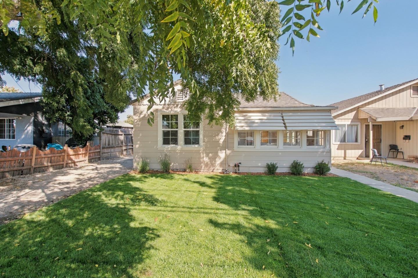 Beige single-story home with an enclosed sunroom, broad lawn, and mature shade trees.