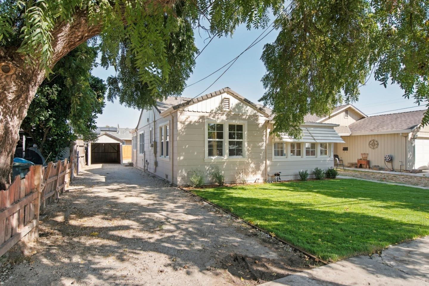 Single-story home framed by mature trees, with a green lawn and gravel driveway.