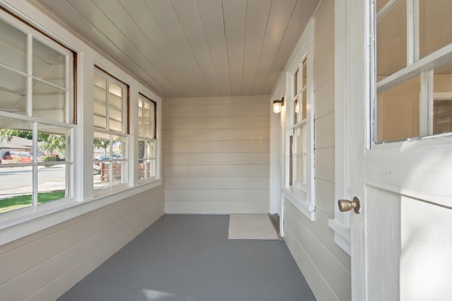 Empty enclosed porch with white paneling, large multi-pane windows, and a gray floor.