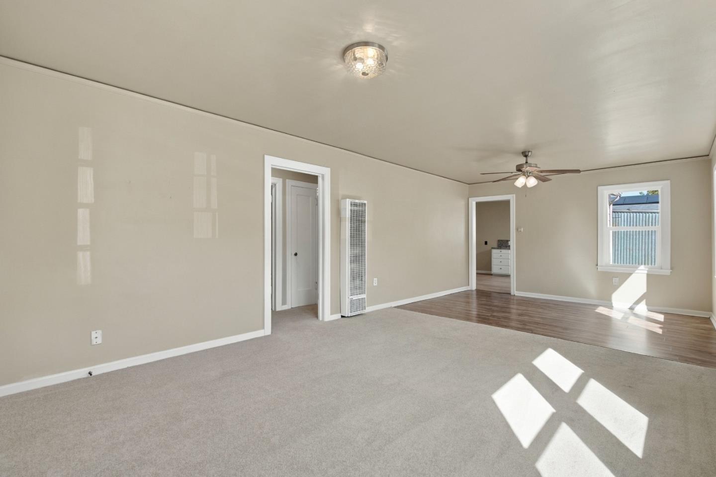Empty living room with carpet, wood-look flooring, a wall heater, and a sunlit window.