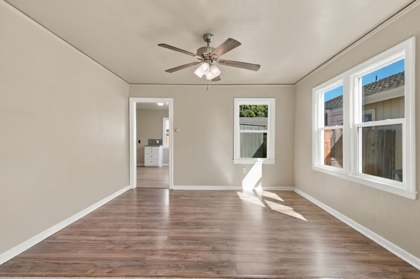 Vacant room with wood-look flooring, ceiling fan, and three white-trimmed windows.