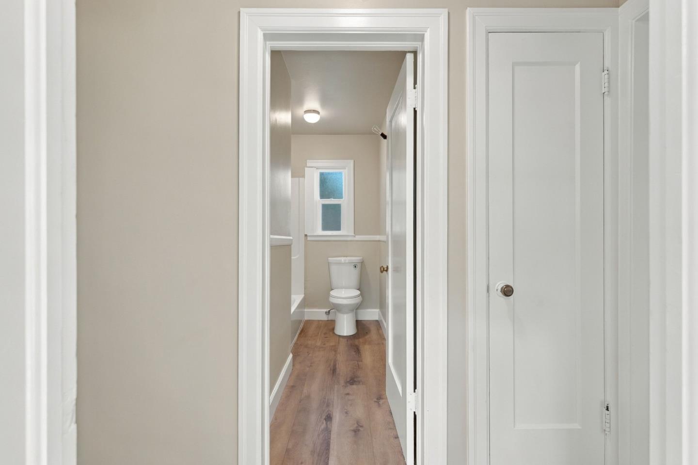 Bathroom with a toilet beneath a small window and wood-look flooring.