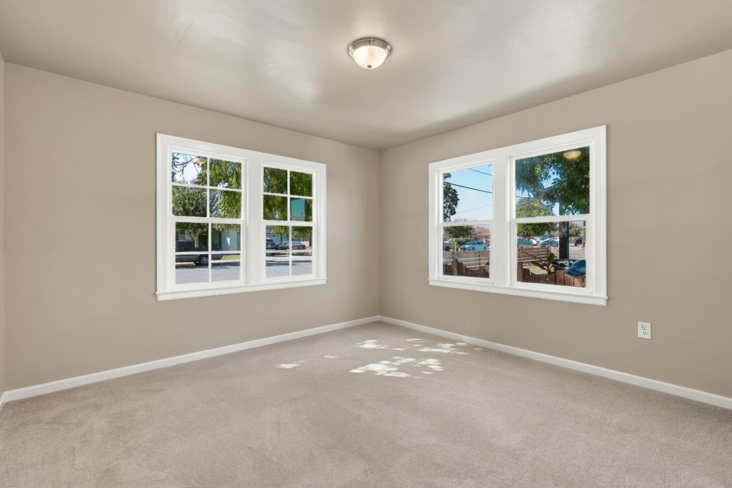 Empty carpeted room with beige walls and two sets of white-trimmed windows.