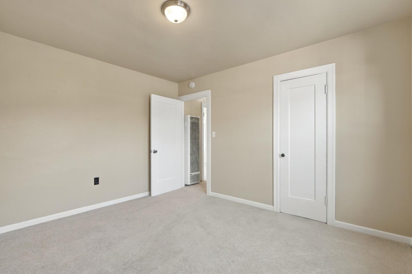 Empty carpeted bedroom with beige walls, two white doors, and a wall heater.