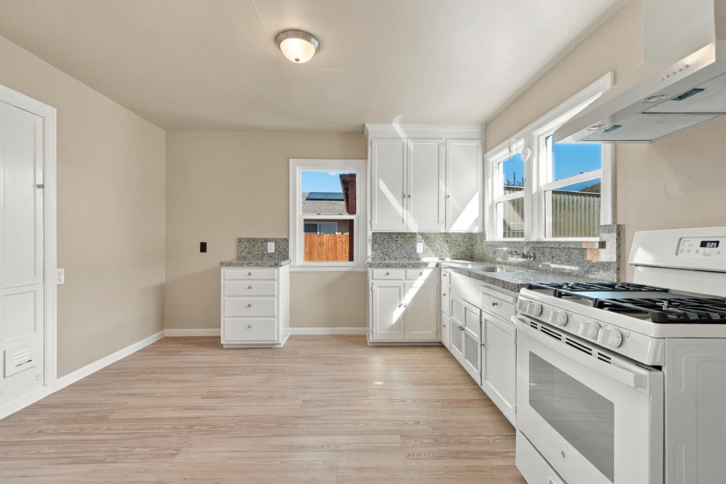 Empty kitchen with white cabinets, speckled counters, a gas range, and sunlit windows.