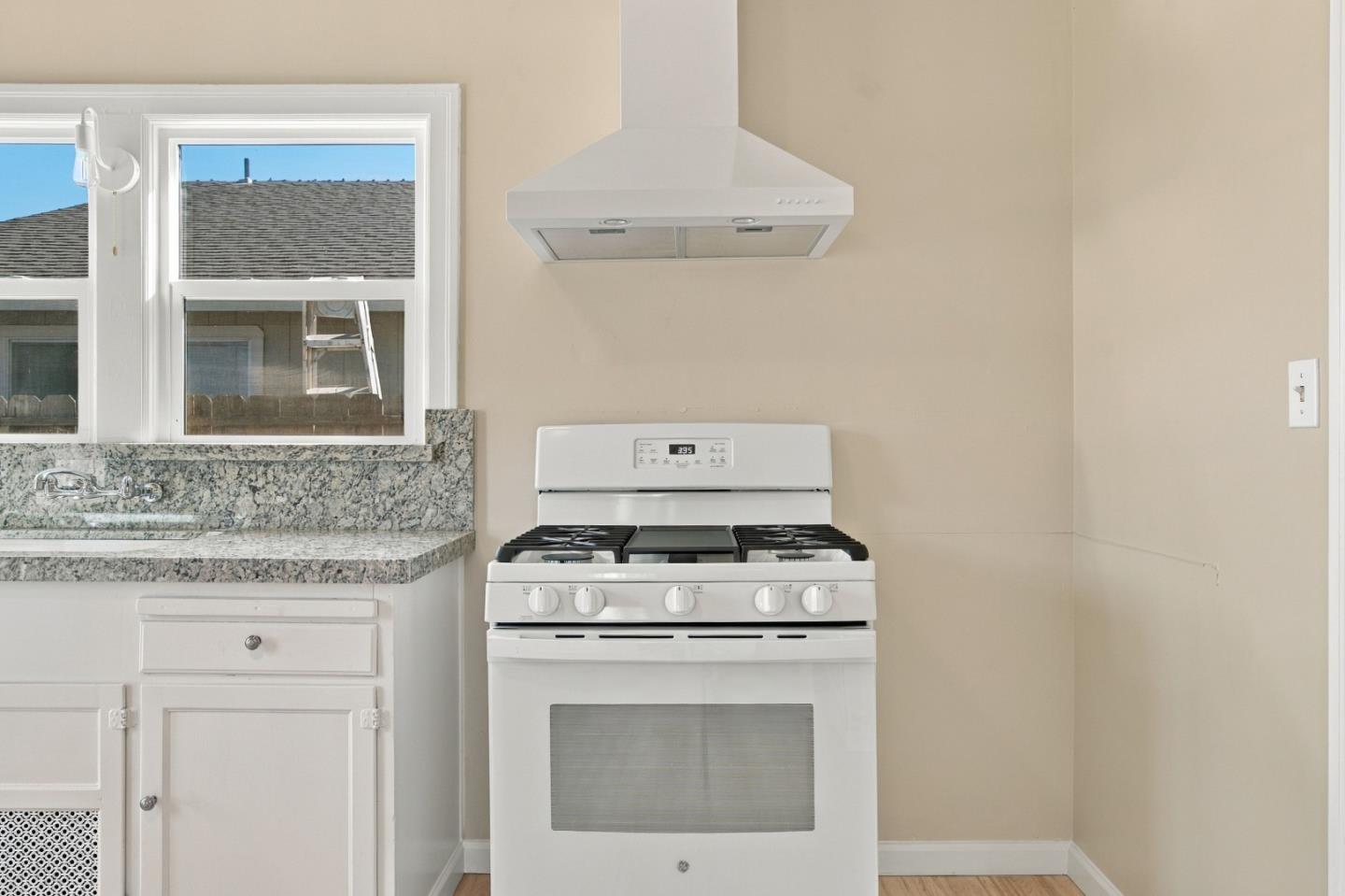 Kitchen with a white gas range and hood, granite countertops, and a window above the sink.