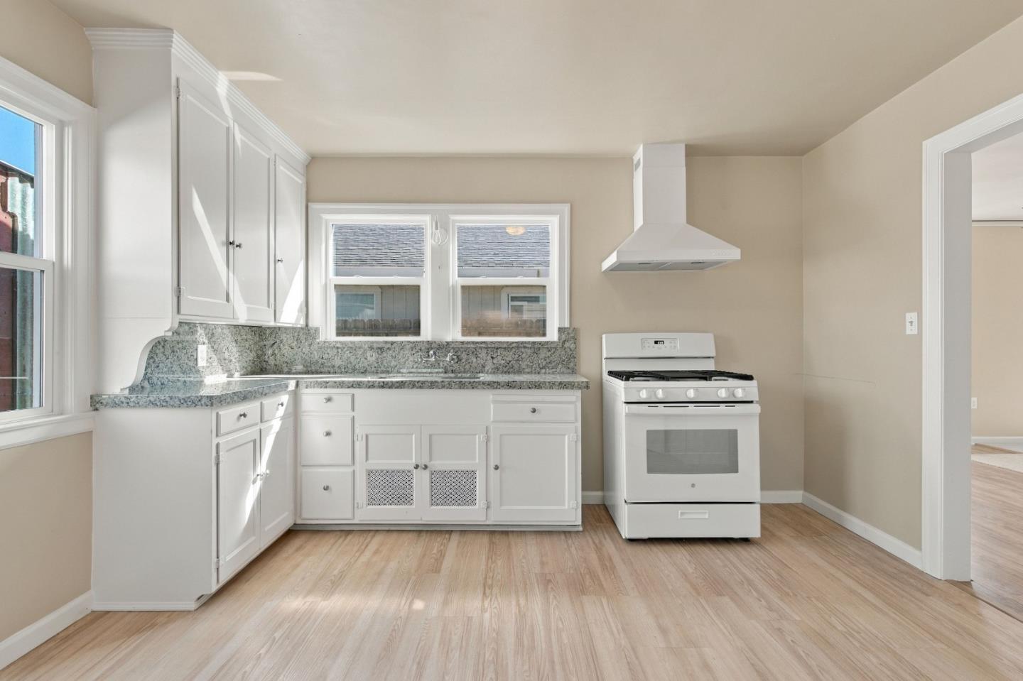 Kitchen with white cabinets, speckled stone counters, and a white range beneath a vent hood.
