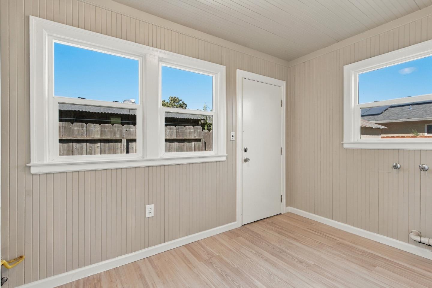 Empty paneled room with light wood flooring, multiple windows, and laundry hookups.