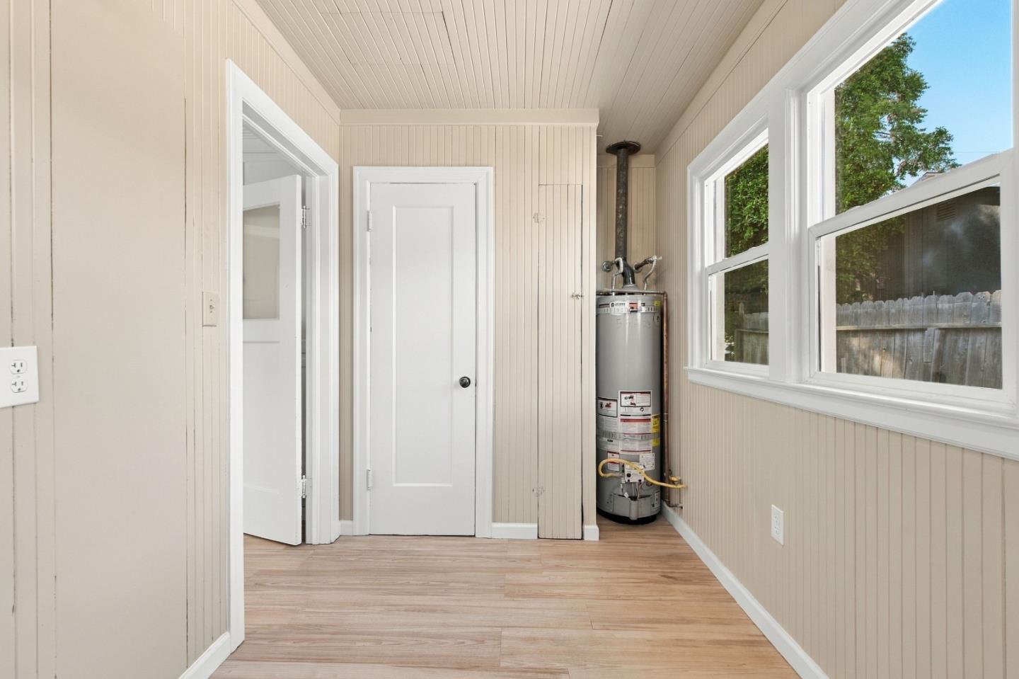 Vacant utility room with a tall water heater, light wood floors, and large windows.