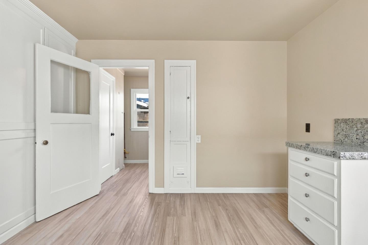 Vacant room with wood-look flooring and granite-topped white drawers beside an open doorway.