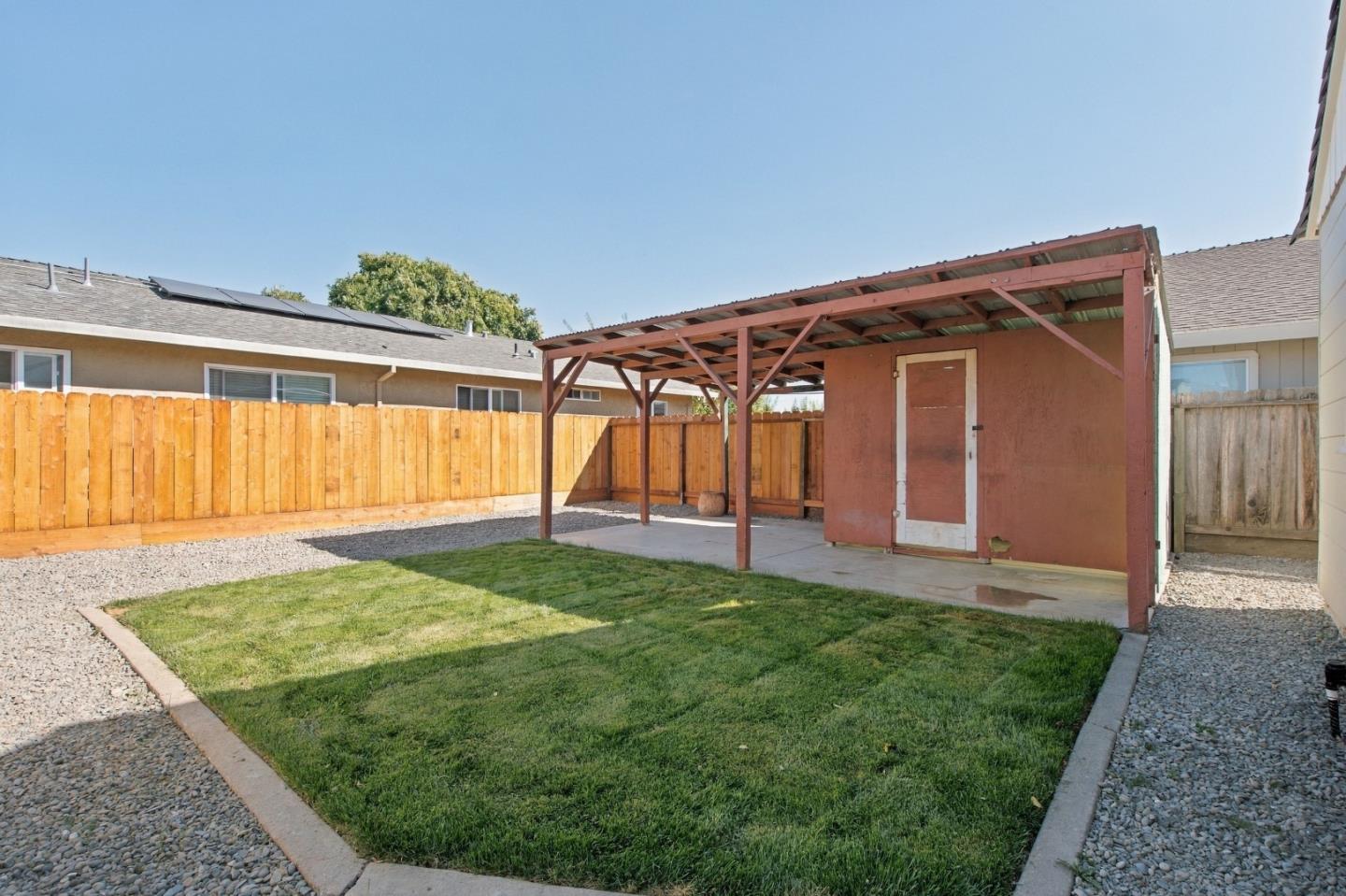 Fenced backyard with a lawn, gravel borders, and a covered patio beside a small shed.