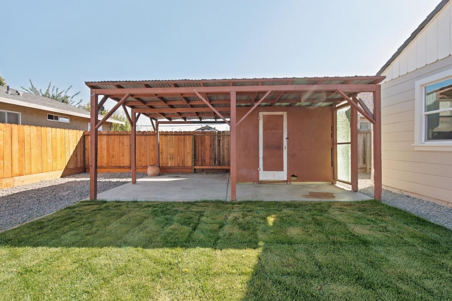 Backyard covered patio with a concrete floor, green lawn, and tall wooden fence.