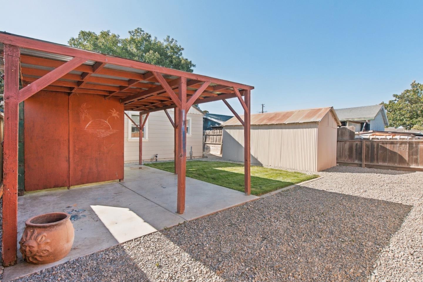 Backyard with a red timber-framed carport, gravel yard, small lawn, and detached metal shed.